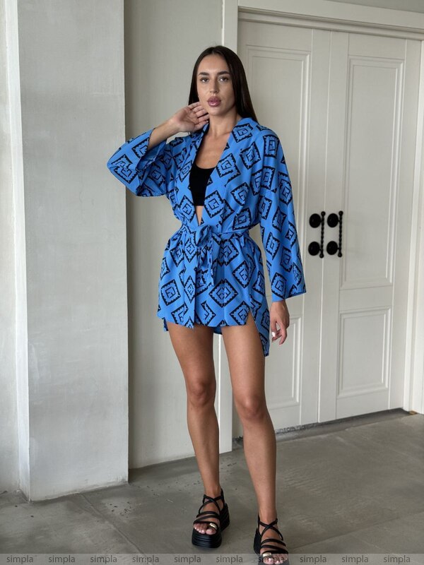 Woman wearing a blue patterned outfit standing in a room with a white door.