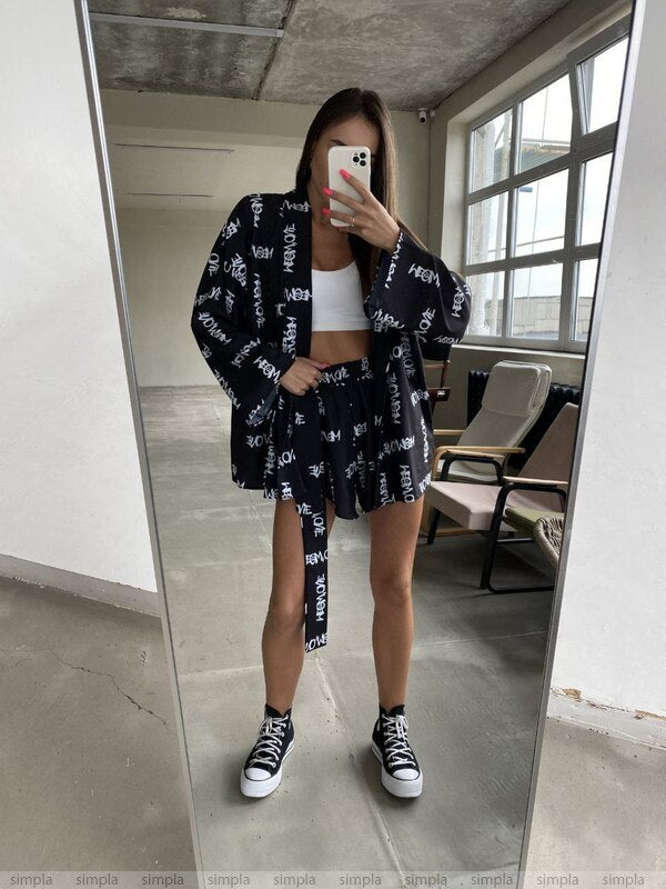 Person wearing a black patterned outfit with white sneakers in a room with large windows.