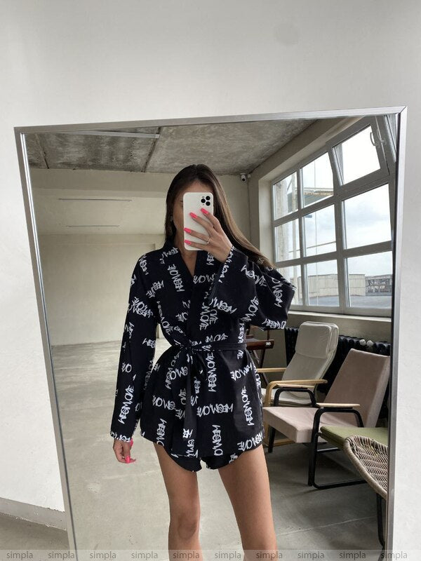 Person wearing a black patterned outfit taking a mirror selfie in an indoor setting.