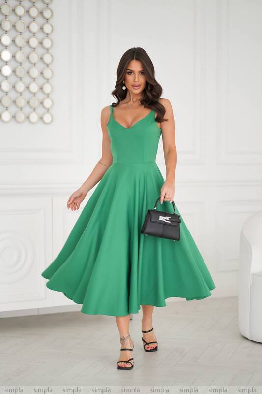 Woman wearing a green dress holding a black handbag in a minimalistic setting