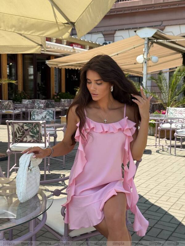 Woman in a pink dress standing outdoors with tables and chairs in the background