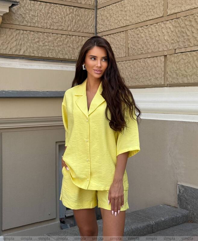 Woman in a yellow outfit standing against a beige wall.