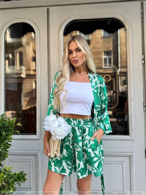 Woman in a green leaf-patterned outfit standing in front of a building entrance.