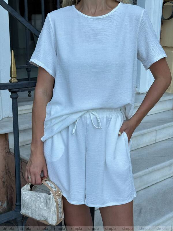 Person wearing a white outfit with shorts and a top, holding a small bag.