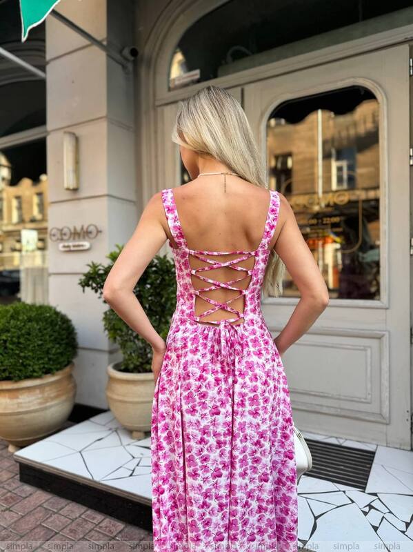 Woman in a pink floral dress standing in front of a building entrance.