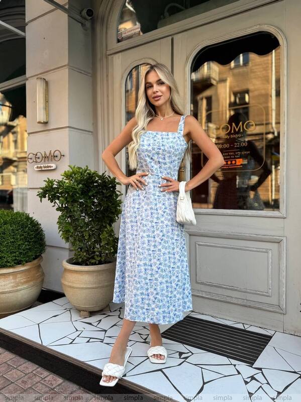 Woman in a light blue dress standing in front of a building entrance.