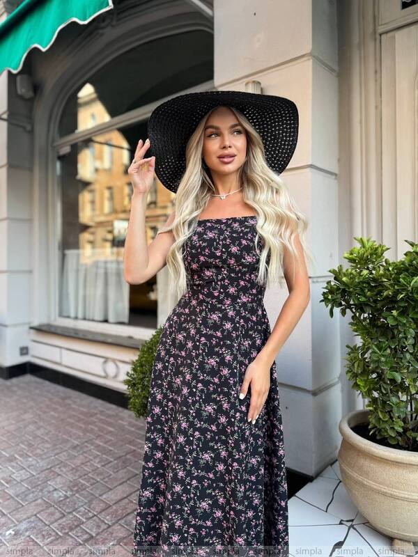 Woman in a floral dress and black hat standing on a city street.
