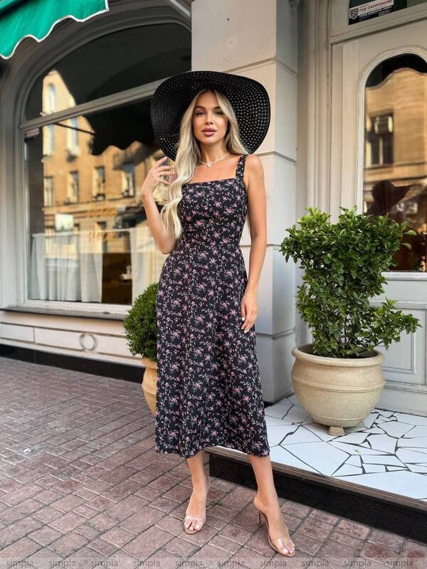 Woman in a floral dress and black hat standing on a city street.