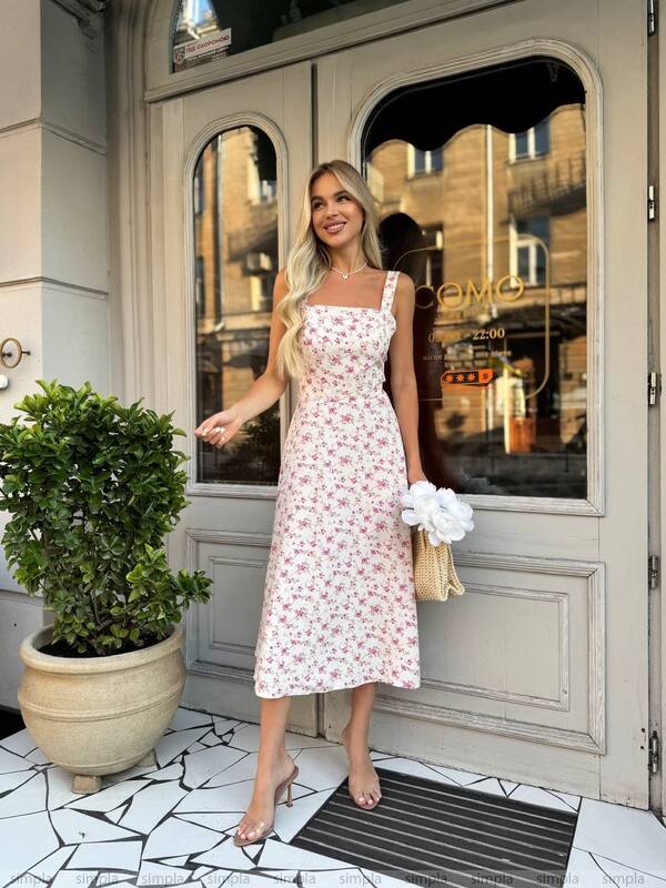 Woman in a floral dress standing in front of a stylish building entrance.