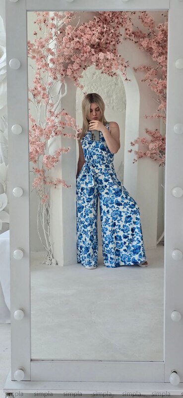 Person wearing a blue floral jumpsuit taking a mirror selfie with cherry blossom decorations.