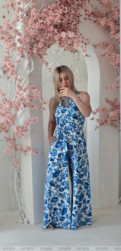 Woman in a blue floral jumpsuit standing in front of pink cherry blossom trees.