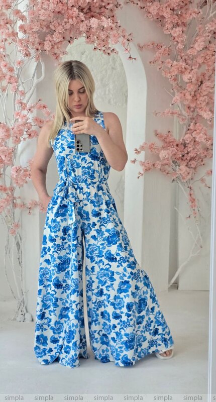 Woman wearing a blue floral jumpsuit in a decorated room with pink flowers.