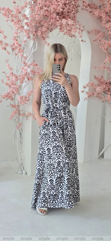Woman taking a mirror selfie wearing a black and white patterned dress with pink floral decorations in the background.