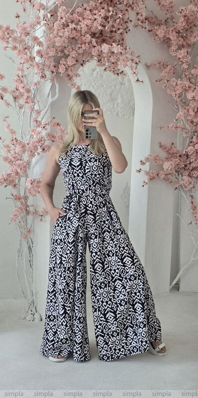 Woman in a black and white patterned dress standing in front of pink floral decorations.