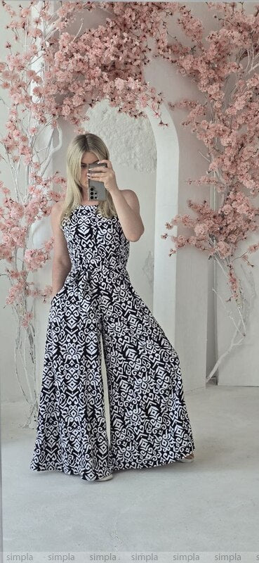 Woman in a black and white patterned dress standing in front of a floral arch.