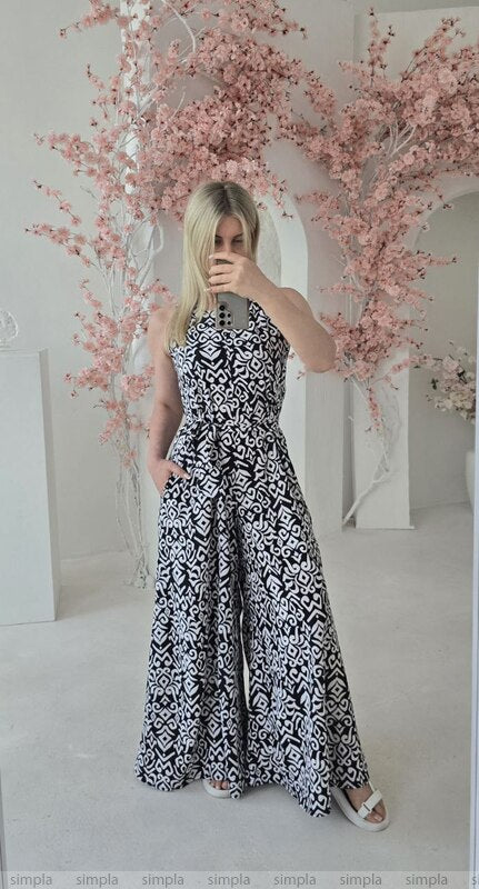 Woman taking a mirror selfie wearing a black and white patterned dress in a decorated room with pink floral arrangements.