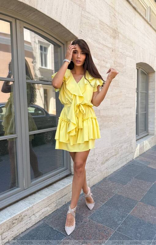 Woman in a yellow dress standing on a sidewalk with a building in the background