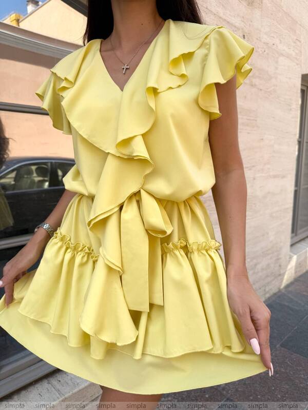 Woman wearing a yellow ruffled dress against a building background