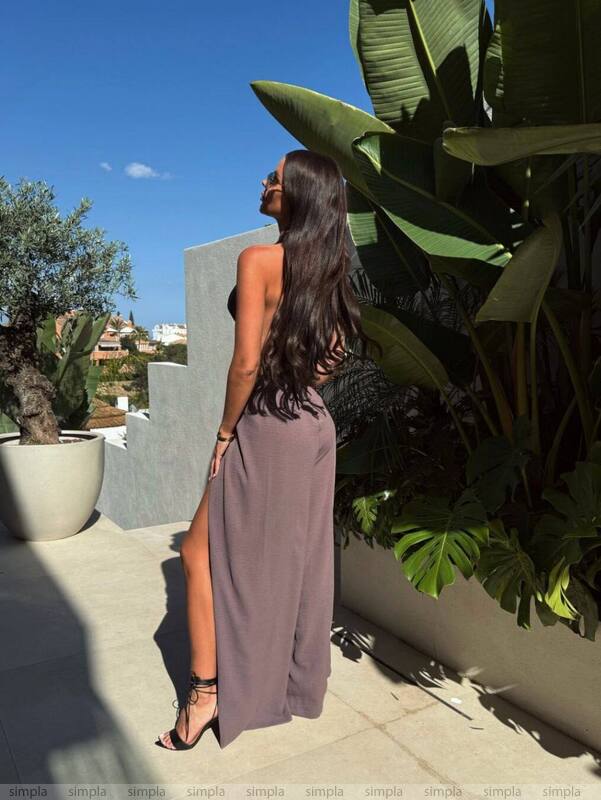 Woman in a long, light-colored dress standing outdoors with plants and a clear sky in the background
