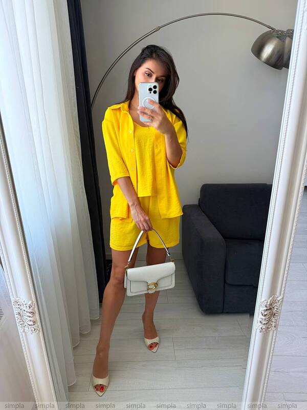 Woman in a yellow outfit taking a mirror selfie in a room with a gray sofa.
