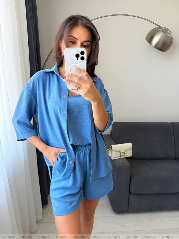 Person wearing a blue outfit taking a mirror selfie in a room with a gray couch and lamp.