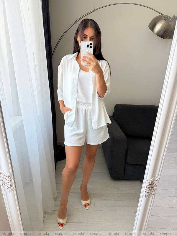 Woman taking a mirror selfie wearing a white outfit in a room with a gray sofa.