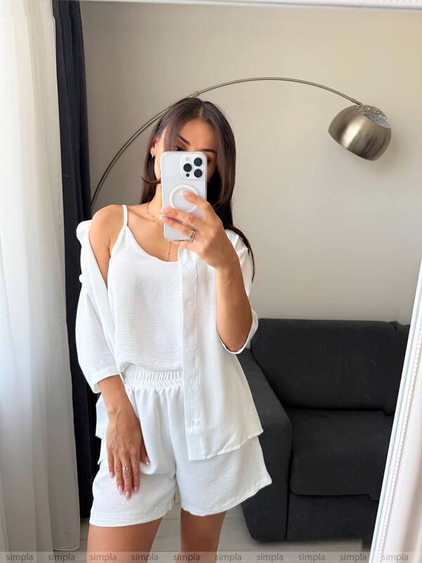 Person taking a mirror selfie wearing a white outfit in a living room.