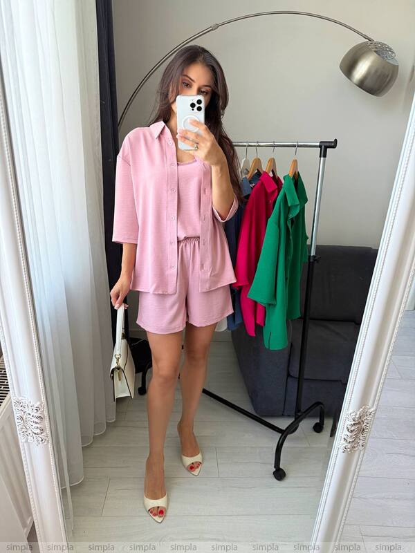 Woman taking a mirror selfie wearing a pink outfit in a room with a clothing rack.