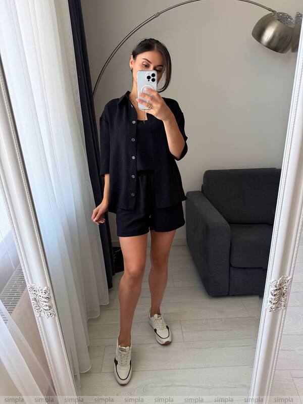 Person taking a mirror selfie wearing a black outfit in a room with a gray sofa.