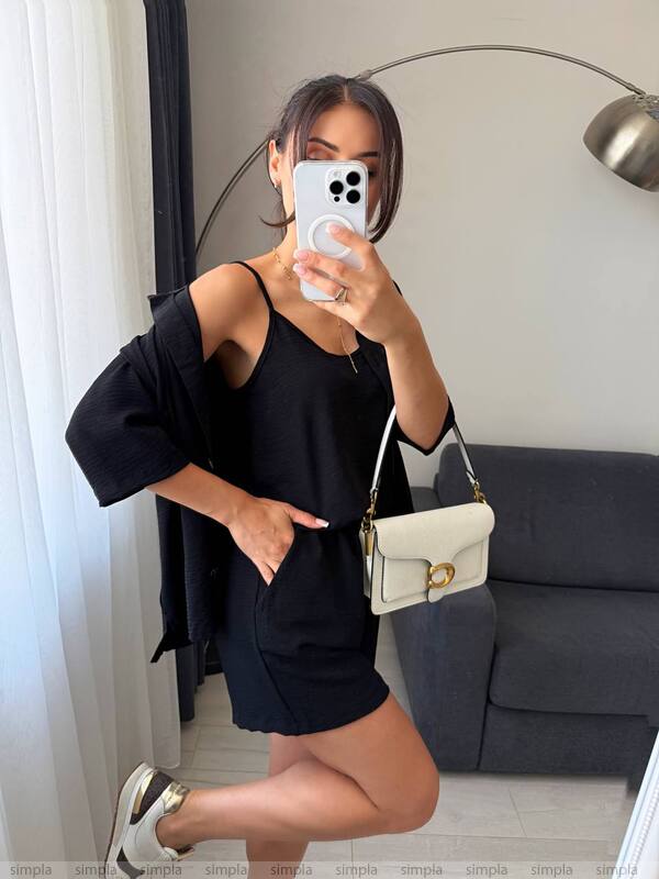 Woman taking a mirror selfie wearing a black outfit with a white handbag in a room.
