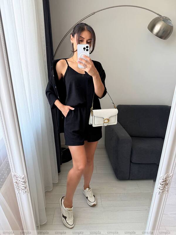 Person taking a mirror selfie wearing a black outfit with a white bag in a room.