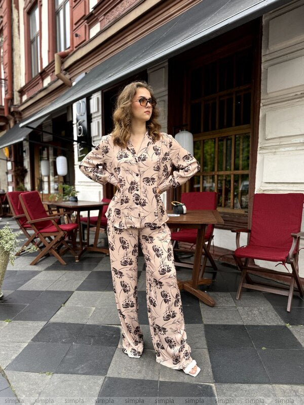 Woman in a floral outfit standing on a street with red chairs and tables.