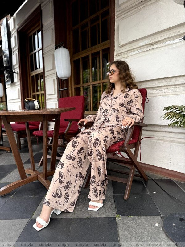 Woman in a floral outfit sitting on a chair outside a building.