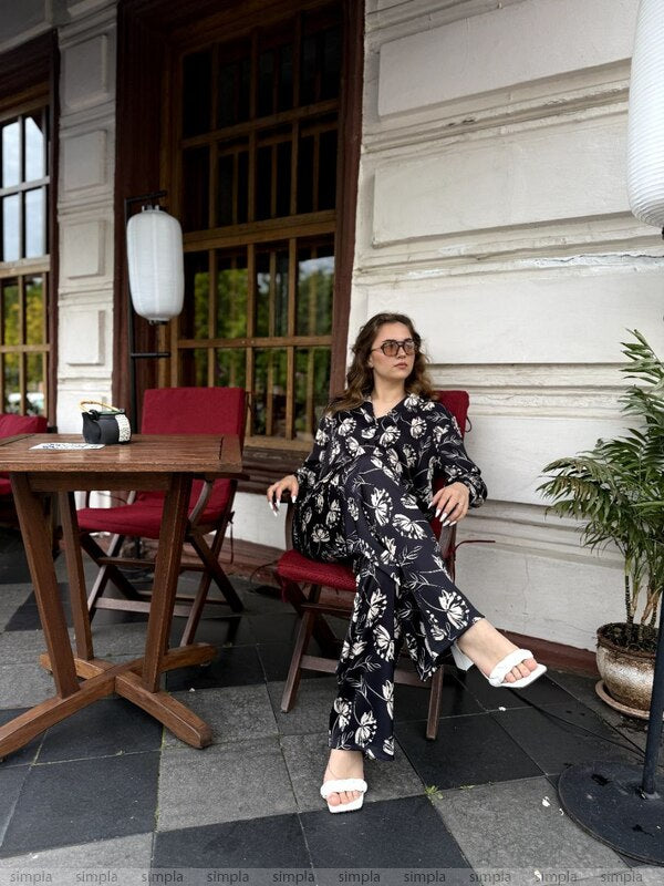 Woman sitting at a table outside a building with red chairs and a plant.