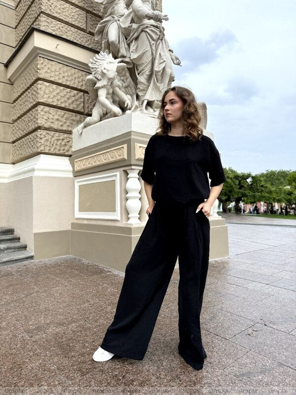Woman in black outfit standing in front of classical statue