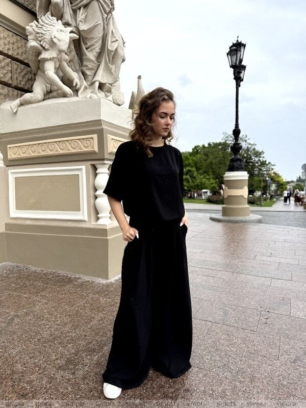 Woman in a black outfit standing in front of classical statues and a lamp post.