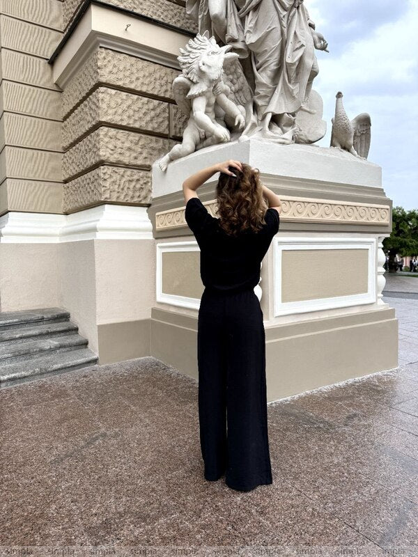 Person in a black outfit standing in front of a large stone statue.