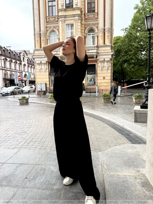 Woman in a black outfit standing on a city street with classical architecture.