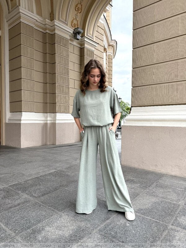 Woman in a light green outfit standing in front of a building with an archway.
