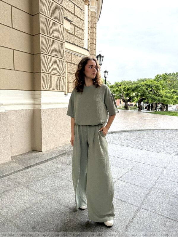 Woman in a green outfit standing outside a building with trees in the background