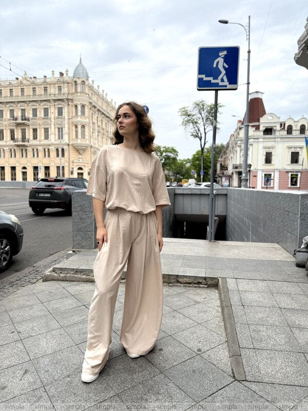 Woman in beige outfit standing on a city street with buildings and traffic lights in the background