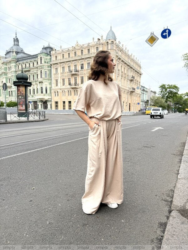 Woman in a beige outfit standing on a city street with classical architecture in the background