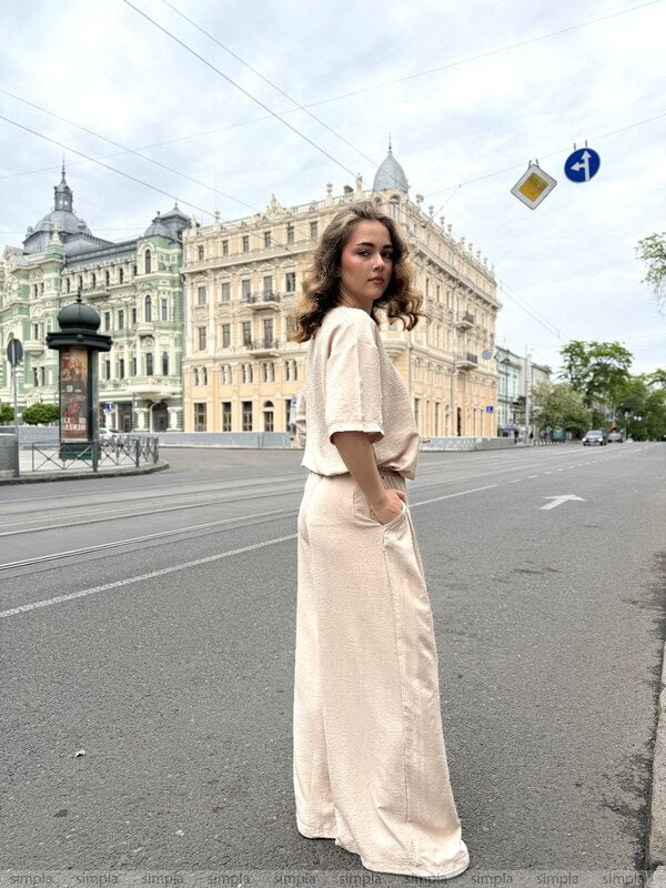 Woman in a long beige dress standing on a city street with classical architecture in the background