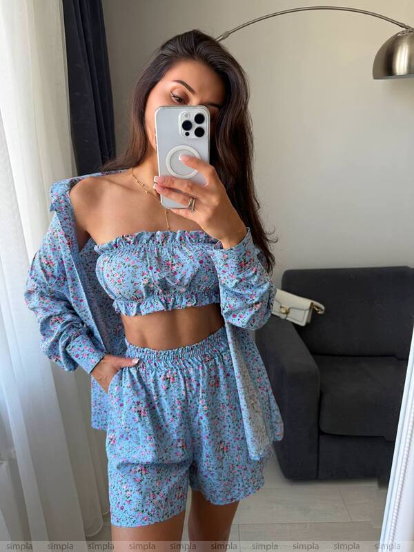 Woman taking a mirror selfie wearing a blue floral outfit in a room.