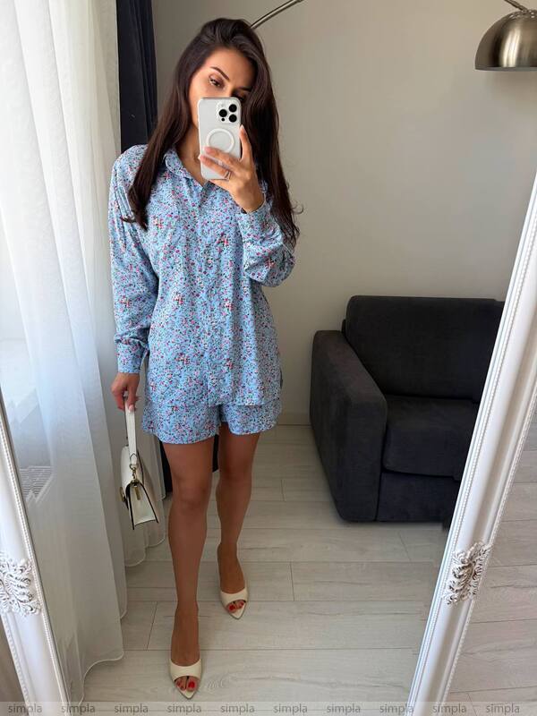 Woman taking a mirror selfie wearing a blue floral dress in a room with a gray sofa.