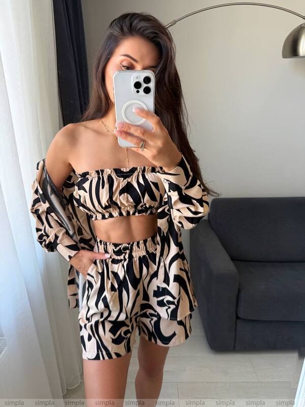 Woman taking a mirror selfie wearing a patterned outfit in a room with a gray sofa.