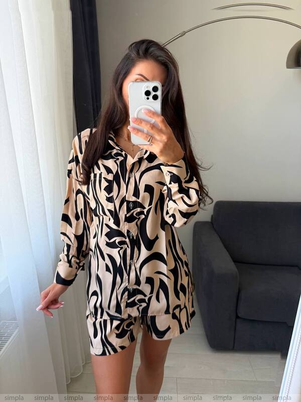 Person wearing a patterned outfit taking a mirror selfie in a room with a gray sofa.