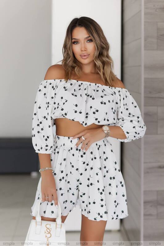 Woman wearing a white off-shoulder dress with black polka dots in an indoor setting.