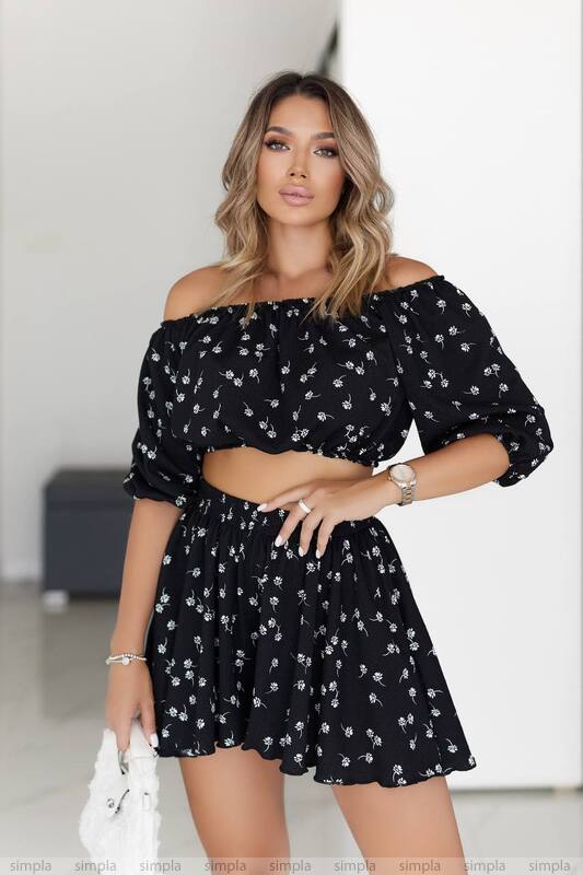 Woman wearing a black floral off-shoulder top and skirt set against a white background