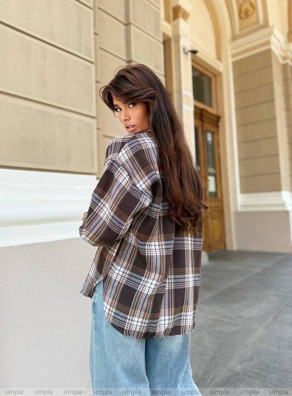 Woman wearing a plaid shirt and jeans standing in front of a building entrance.